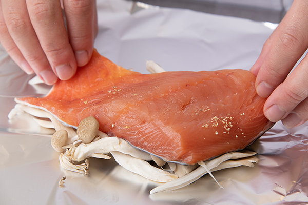 秋鮭の切り身に塩コショウをする。アルミホイルに小房にしたしめじ、まいたけを敷き、その上に鮭の切り身を置く。