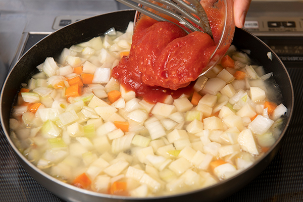 フライパンでさいの目切りにした玉ねぎ、にんじん、じゃがいもをさっと炒め、水、トマト水煮をいれて15分煮る。